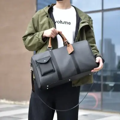 Homme portant un sac de voyage en cuir noir avec poignées marron, parfait pour un look urbain décontracté — idéal pour les week-ends ou voyages courts.