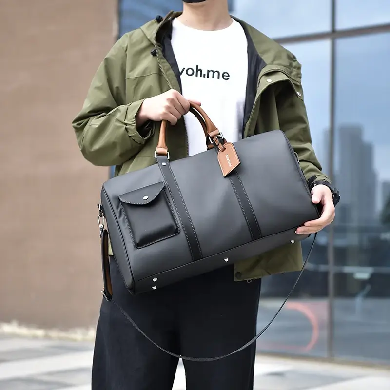 Homme portant un sac de voyage en cuir noir avec poignées marron, parfait pour un look urbain décontracté — idéal pour les week-ends ou voyages courts.