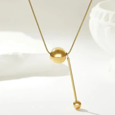 Collier en acier inoxydable doré avec pendentif bille et barre pendante — finition brillante et design épuré, idéal pour sublimer une tenue sobre ou habillée.