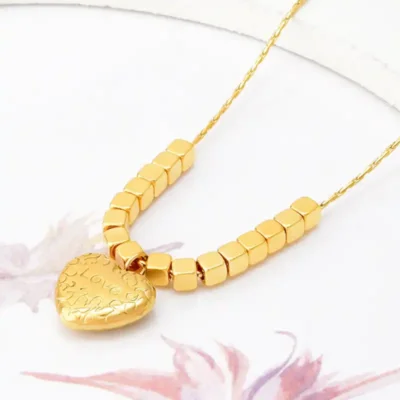 Collier doré avec pendentif cœur gravé « Love », entouré de perles cubiques — idéal pour un look romantique et délicat, parfait en cadeau d’amour ou d’anniversaire.