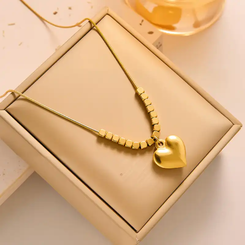 Collier doré avec pendentif cœur et perles carrées, présenté dans une boîte cadeau beige — idéal comme présent pour elle, à l’occasion d’un anniversaire, la Saint-Valentin ou la fête des mères.