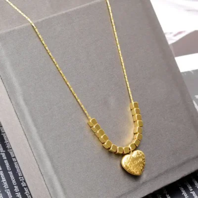 Collier fin en or avec pendentif cœur gravé « Love » et perles carrées — présenté sur un support élégant, idéal comme cadeau pour elle, pour la Saint-Valentin ou une déclaration d’amour.