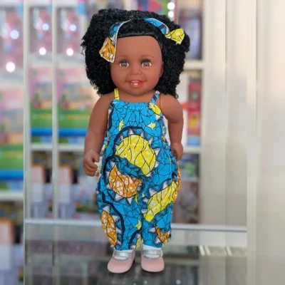 Poupée noire avec salopette imprimée style africain et bandeau assorti — célébrant la diversité culturelle tout en stimulant l’imagination des enfants.
