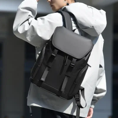 Homme portant un sac à dos transfrontalier gris, associé à une veste légère — look urbain moderne, parfait pour les déplacements en ville, au bureau ou en voyage.