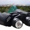 Jumelles 20x50 HD utilisées pour observer un paysage urbain — effet de zoom visible dans l’oculaire (bâtiment agrandi), démontrant leur puissance de grossissement et netteté HD.