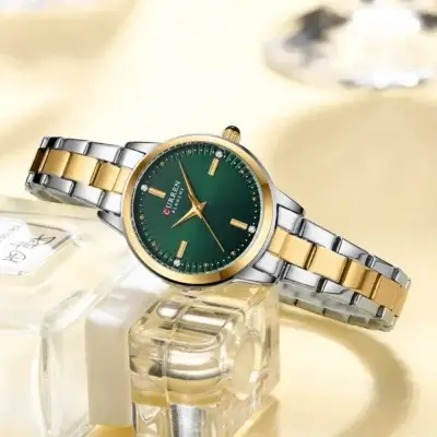 Montre femme Curren 9094 élégante, cadran vert émeraude avec index dorés et strass, bracelet acier bicolore or/argent — présentée sur un flacon de parfum pour un look raffiné et féminin.