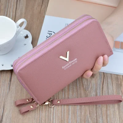 Portefeuille femme long en rose poudré, double zip doré, logo « Sweet Dream » et poignée détachable — style doux et féminin, idéal pour un look chic et organisé.