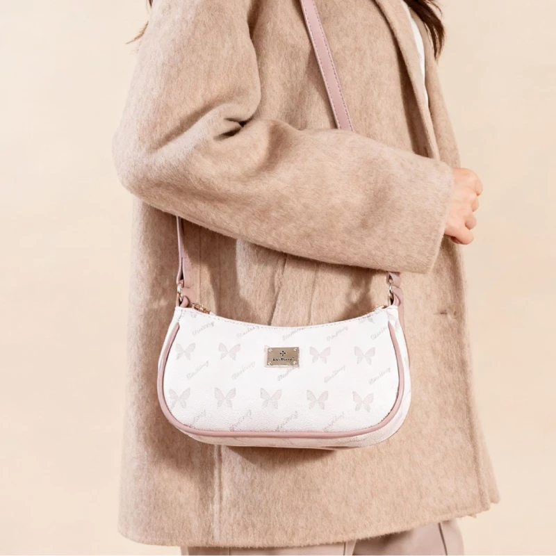 Petit sac à main baguette à motif papillon rose porté à l'épaule sur un manteau beige, style chic et féminin.