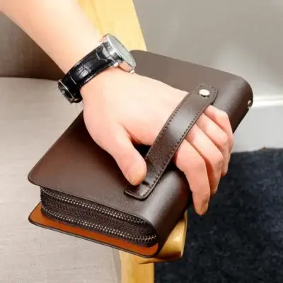 Main masculine tenant une pochette en cuir marron foncé, accessoire business assorti à une montre.