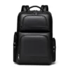 Sac à dos professionnel en simili-cuir noir texturé posé sur un tabouret en bois, mettant en valeur les multiples compartiments zippés et la poignée supérieure.