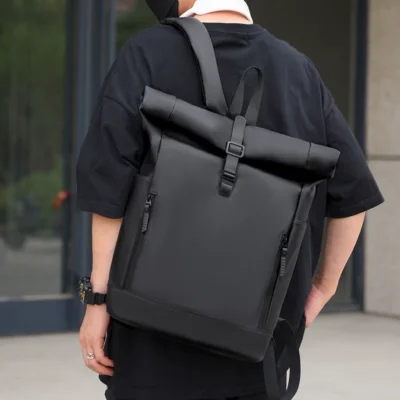 Homme portant un sac à dos noir étanche sur le dos, idéal pour le travail ou l'université, style casual.