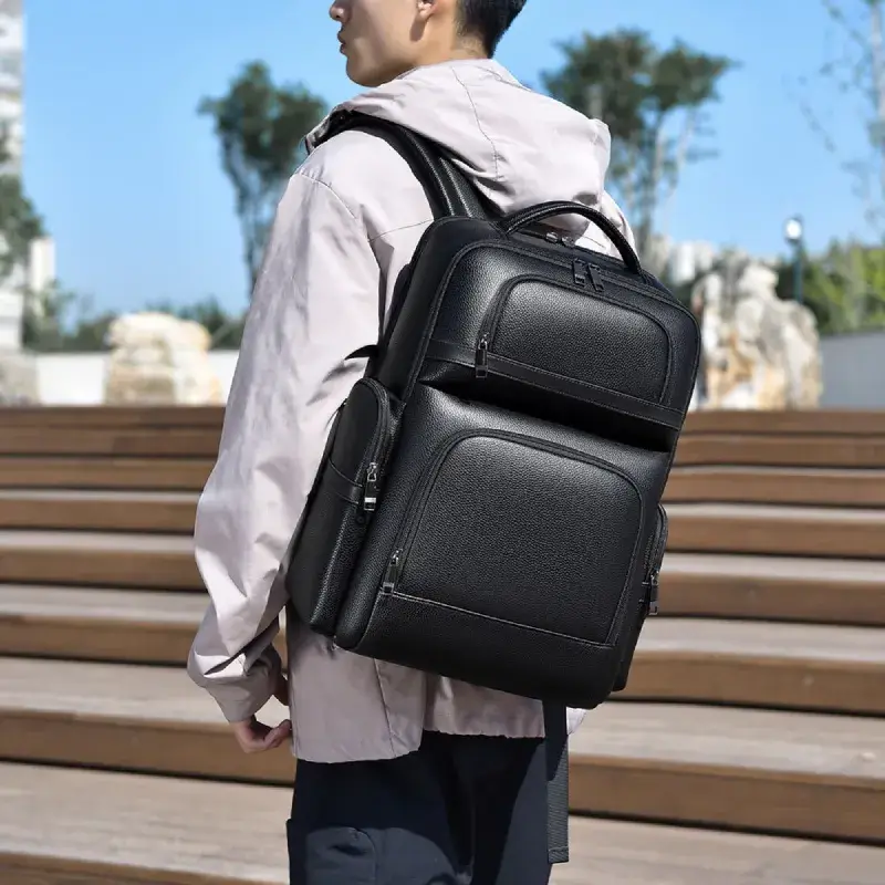 Homme portant le sac à dos noir haut de gamme en extérieur, vue arrière montrant l'ajustement des bretelles et le style urbain moderne.