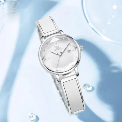 Vue rapprochée de la montre OLEVS 5656 sur fond bleu clair avec cristaux, mettant en valeur le cadran facetté lumineux et la qualité du bracelet métal.