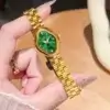 Montre femme OLEVS 5666 dorée tenue à la main, mettant en valeur le cadran vert émeraude unique avec chiffres romains et cristaux scintillants.