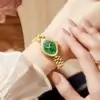 Montre de luxe OLEVS 5666 portée au poignet par une femme, design doré et cadran vert distinctif, accessoire de mode raffiné et élégant.