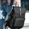 Détail du sac à dos business noir tenu à la main, mettant en valeur la texture du matériau résistant à l'eau et la robustesse de la poignée de transport.