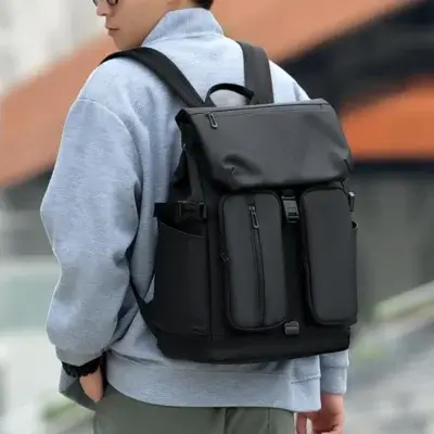 Vue arrière d'un homme portant le sac à dos noir roll-top avec poches avant multiples et boucles de serrage, style streetwear moderne — sac à dos grande capacité imperméable adapté aux jeunes actifs et étudiants.