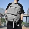 Homme portant un sac à dos ordinateur portable gris avec poches en filet et tirettes orange, design décontracté et étanche, idéal pour le lycée, l'université ou les voyages urbains.