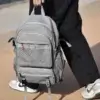 Personne tenant le sac à dos ordinateur par sa poignée supérieure robuste, mettant en valeur le design moderne avec détails orange et la grande capacité de rangement pour le quotidien.