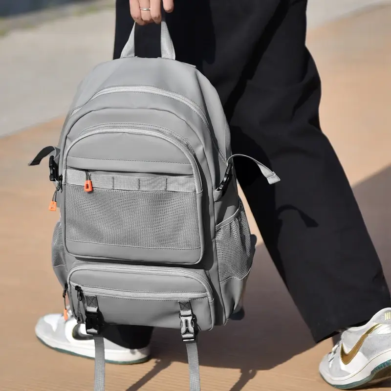Personne tenant le sac à dos ordinateur par sa poignée supérieure robuste, mettant en valeur le design moderne avec détails orange et la grande capacité de rangement pour le quotidien.