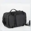 Sac à dos rétro noir posé à l'horizontale en mode sacoche de voyage, montrant les deux grandes poches avant zippées, les poignées de transport et le design polyvalent imperméable avec port USB.
