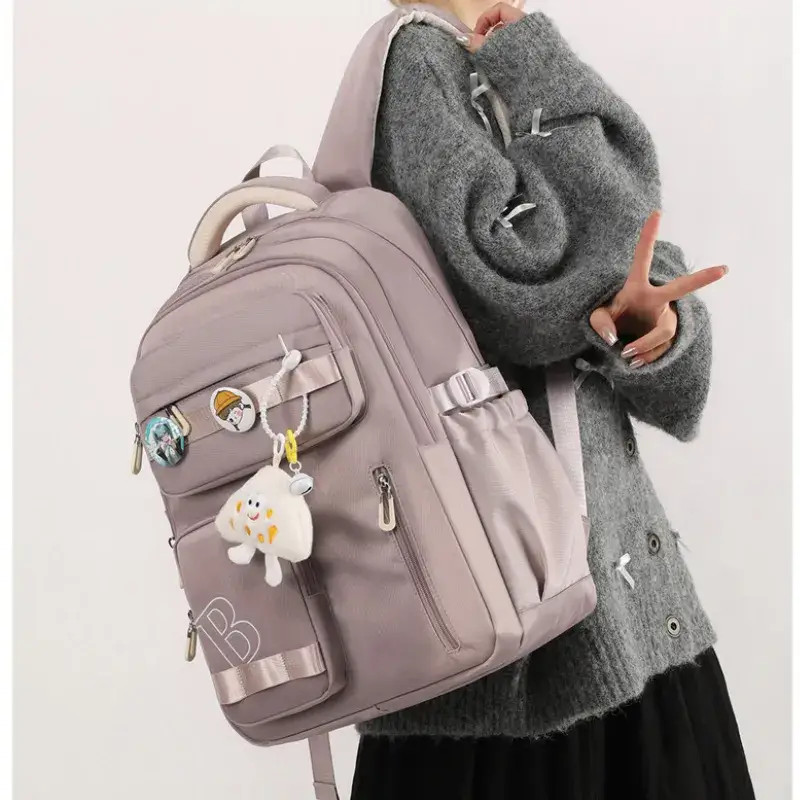 Jeune fille portant un sac à dos scolaire ergonomique violet clair (mauve) avec porte-clés peluche nuage et badges décoratifs, design tendance et spacieux pour le collège ou le lycée.