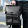 Homme tenant le sac à dos business noir à motif monogramme par sa poignée supérieure en extérieur, mettant en valeur la grande capacité, le style urbain et la praticité pour les déplacements professionnels.