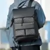 Homme portant un sac à dos business gris et noir à motif damier sur le dos, style urbain et décontracté avec veste bleue, idéal pour les trajets quotidiens et le transport d'ordinateur 16 pouces.
