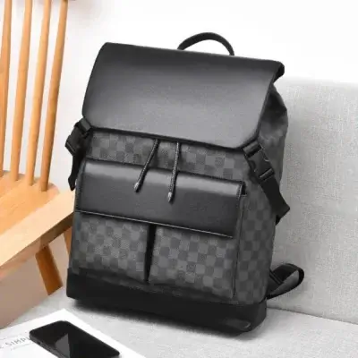 Sac à dos business homme motif damier posé sur un canapé gris à côté d'un smartphone, montrant le design moderne avec rabat, cordon de serrage et multiples poches de rangement pour le quotidien.