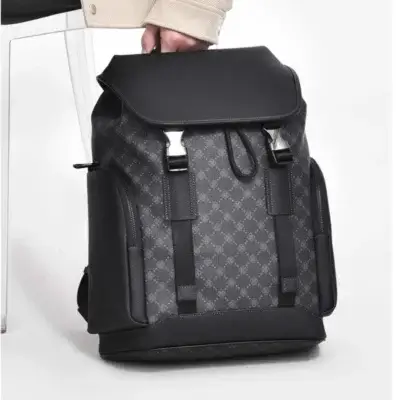 Sac à dos homme business tenu par la poignée supérieure, montrant le rabat en cuir synthétique, les boucles de fermeture et le motif discret, parfait pour les déplacements professionnels et les voyages