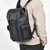 Homme portant le sac à dos ordinateur noir à motif monogramme sur le dos, style casual et urbain avec veste beige — sac imperméable grande capacité idéal pour le bureau, les voyages et le quotidien.