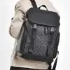 Homme portant le sac à dos voyage business noir à motif monogramme sur l'épaule, design élégant avec poches latérales zippées et sangles à boucles, idéal pour transporter un ordinateur 16 pouces au quotidien.