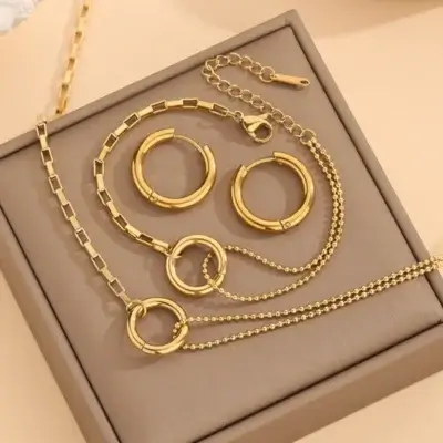Parure complète 3 pièces dorée anti-ternissement comprenant collier à double chaîne, bracelet assorti et boucles d'oreilles créoles, tous ornés d'un motif anneau circulaire — set de bijoux femme élégant présenté sur écrin, parfait pour un cadeau.