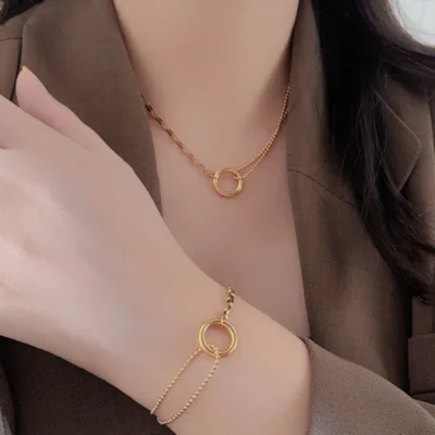 Femme portant un ensemble de bijoux dorés anti-ternissement avec collier et bracelet assortis à motif anneau circulaire, chaînes mixtes maille plate et perles — parure élégante et minimaliste parfaite pour un look chic et moderne.