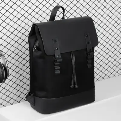 Sac à dos noir en tissu Oxford posé sur fond de grille métallique avec un casque audio à côté, mettant en valeur son design minimaliste et moderne — sac de voyage pratique et tendance pour jeune actif et étudiant.