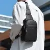 Sacoche bandoulière homme noire portée dans le dos sur une chemise blanche.