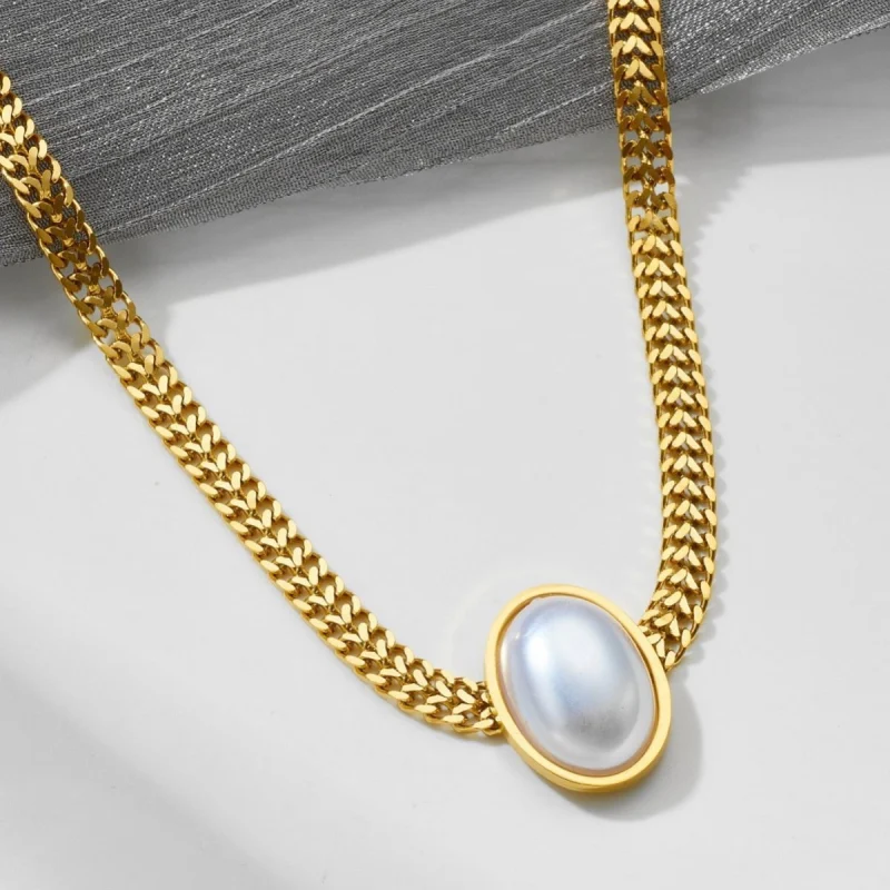 Gros plan sur un collier plaqué or style bohème vintage avec chaîne maille épaisse et grand pendentif ovale en cristal blanc nacré — bijou élégant et raffiné pour femme, parfait pour une tenue de soirée ou un look chic.