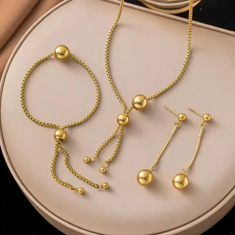Ensemble de bijoux tendance en acier inoxydable plaqué or comprenant collier à perles avec pampilles, bracelet assorti et boucles d'oreilles pendantes — parure femme élégante et moderne, idéale en cadeau ou pour une occasion spéciale.